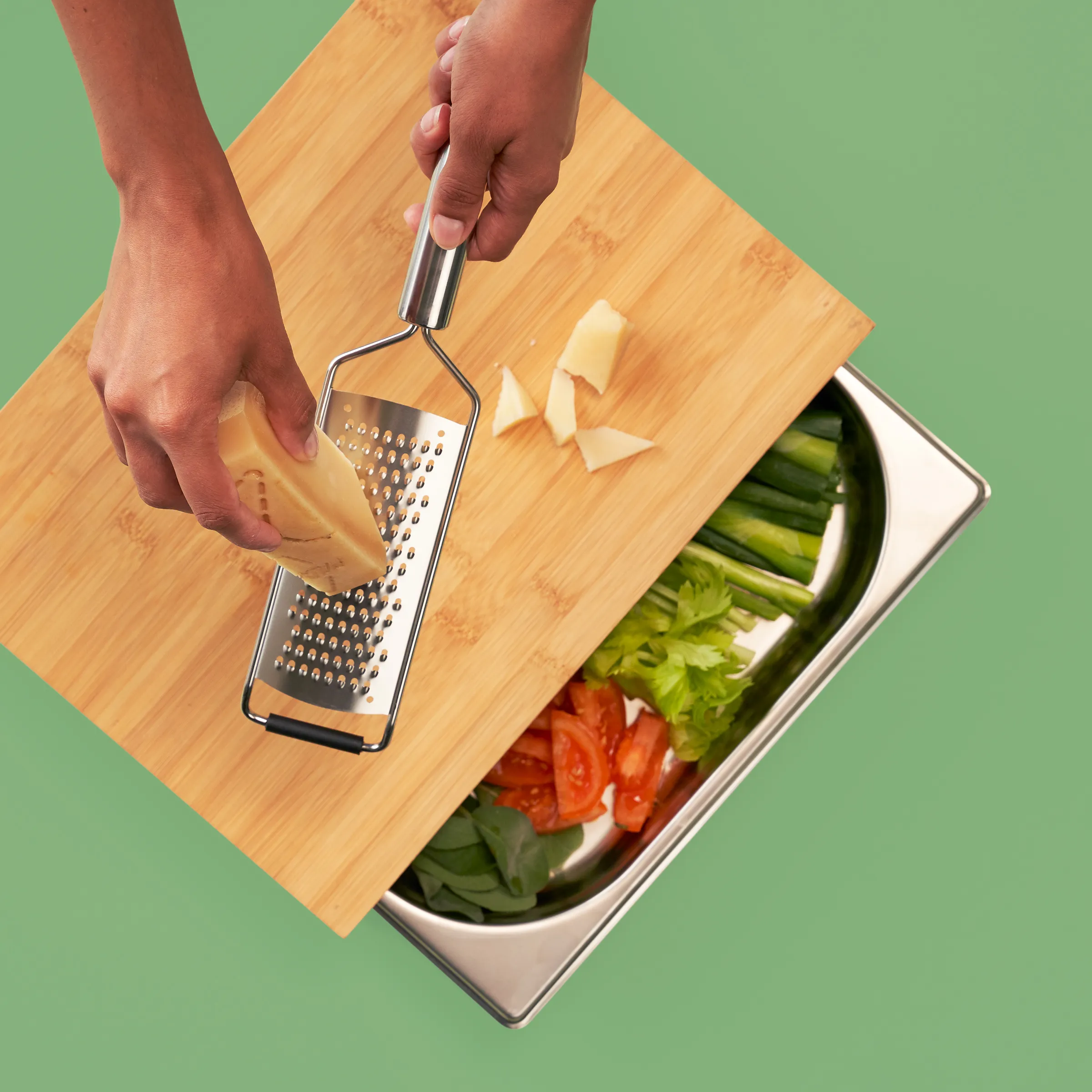 Käsereibe und Gemüseschale - frischer Salat zubereiten Hände reiben Käse auf Schneidebrett über Gemüseschale mit Salat, Tomaten und Gurken