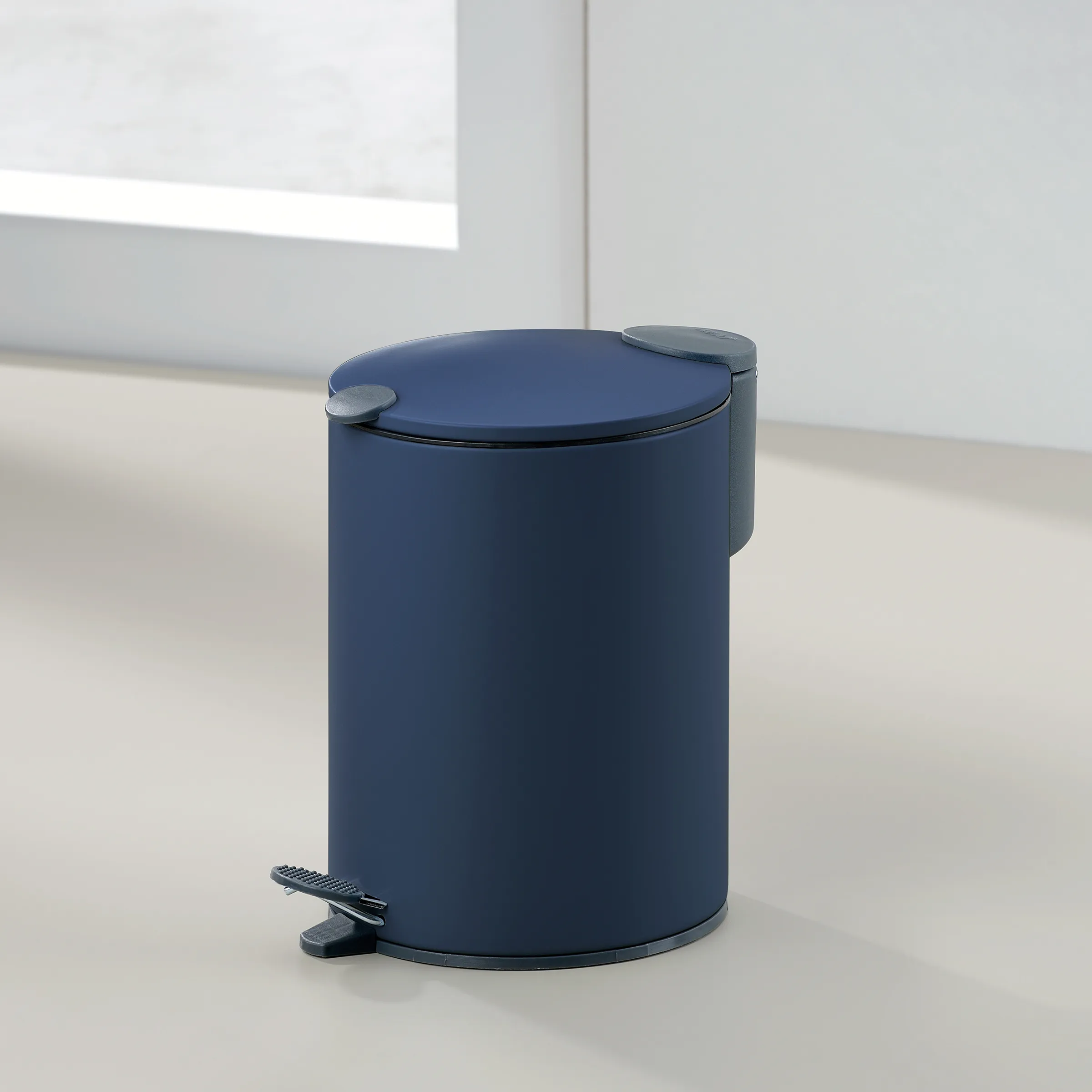 Dunkelblauer Tretmülleimer mit Deckel und Fußpedal in minimalistischem Design auf hellem Fliesenboden