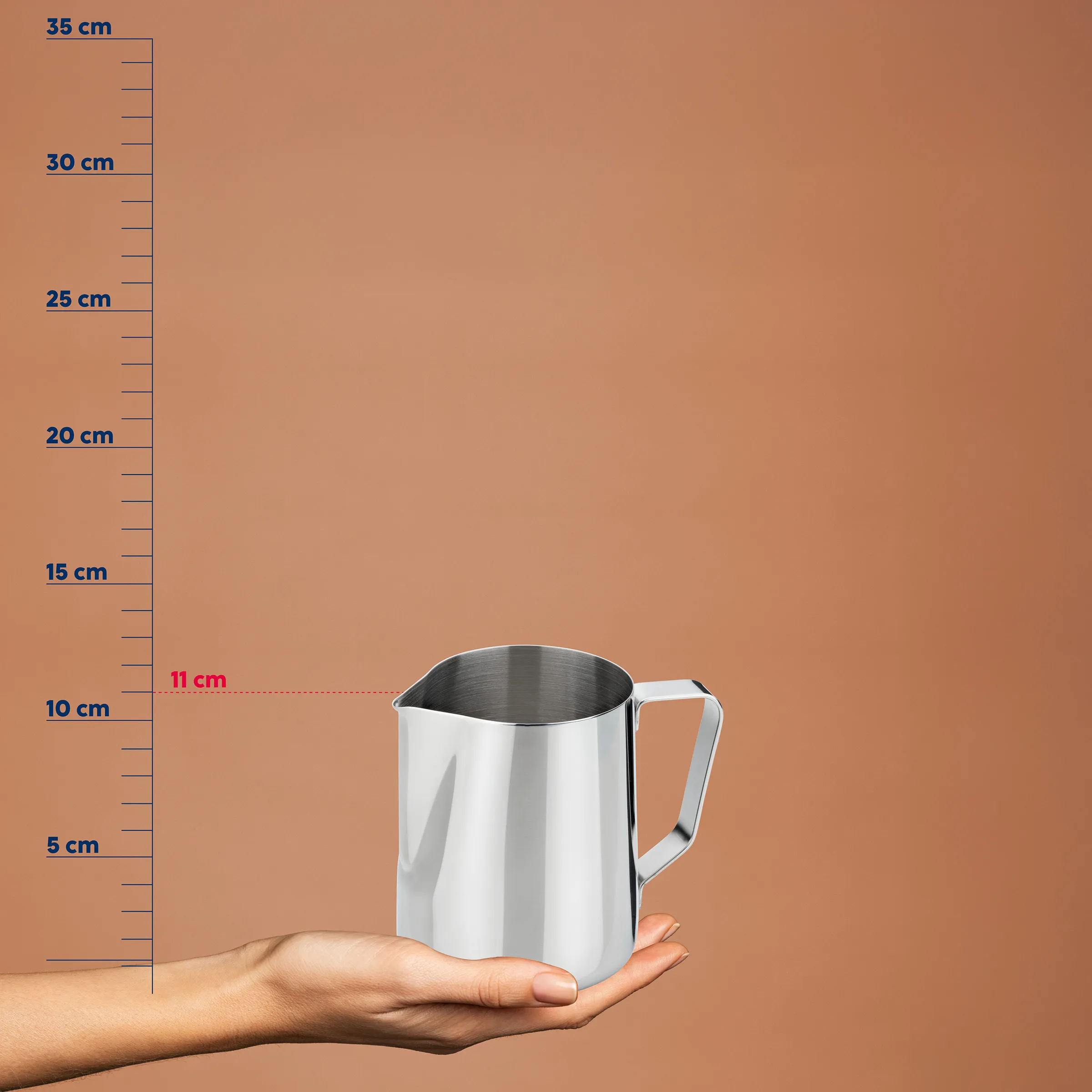 Edelstahl-Milchkännchen mit Messskala wird in einer Hand gehalten, Größenvergleich zeigt 11 cm Breite