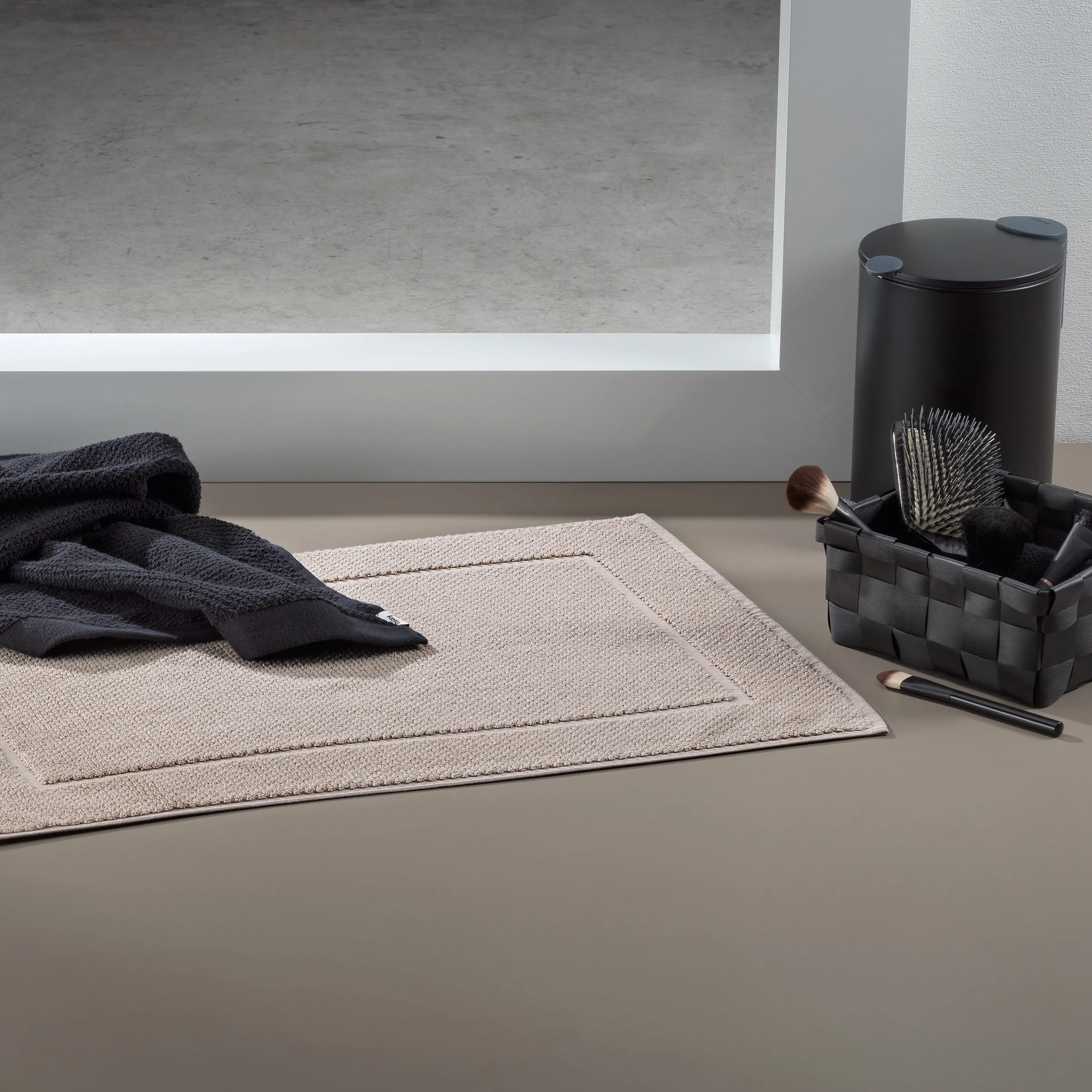 Badezimmer Accessoires Set - Minimalistisch & elegant Minimalistisches Badezimmer-Set mit beigem Handtuch, schwarzem Behälter, Haarbürste und Kosmetikpinsel auf grauem Tablett