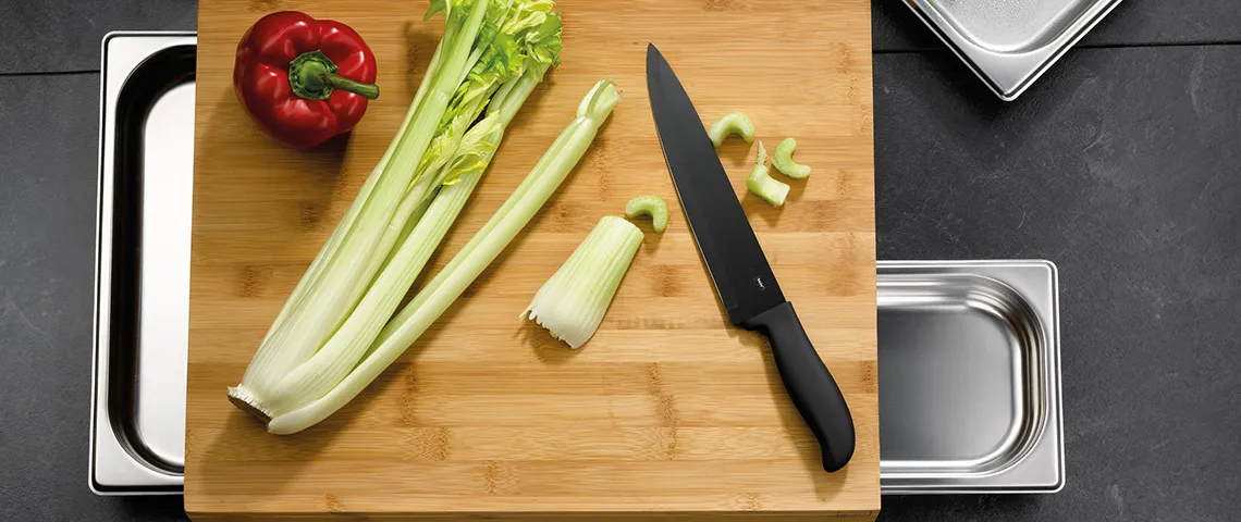 Gemüse schneiden - Kochmesser und Zutaten auf Schneidebrett Holzbrett mit frischen Zutaten: rote Paprika, Stangensellerie, schwarzes Messer und Schüsseln zur Vorbereitung