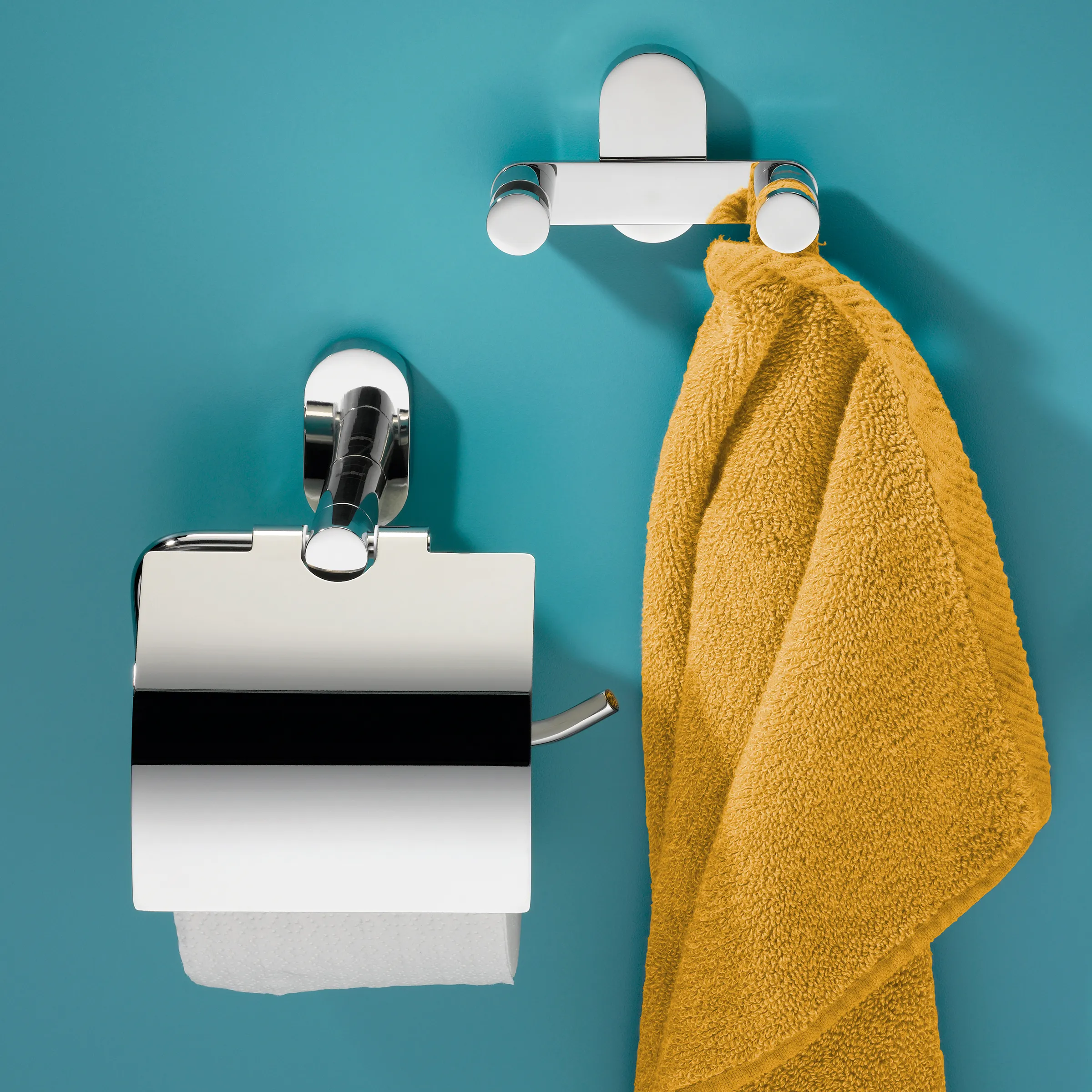 Badezimmer Accessoire Set - Toilettenpapierhalter und Handtuchhaken verchromt Modernes Badezimmer-Set mit verchromtem Toilettenpapierhalter und Handtuchhaken mit gelbem Handtuch an türkiser Wand
