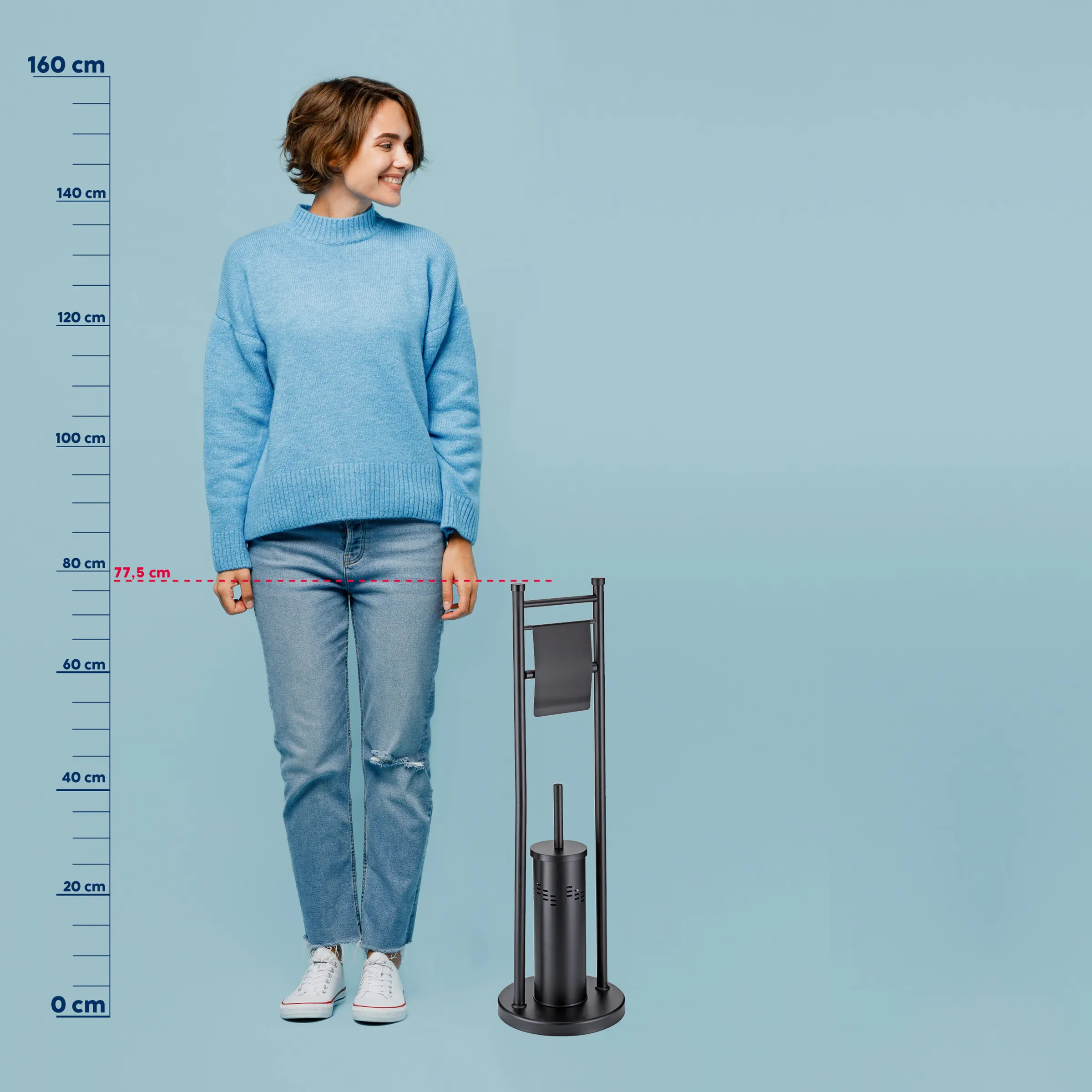 Junge Frau in blauem Pullover und Jeans neben schwarzem Toilettenpapierhalter mit Maßstab