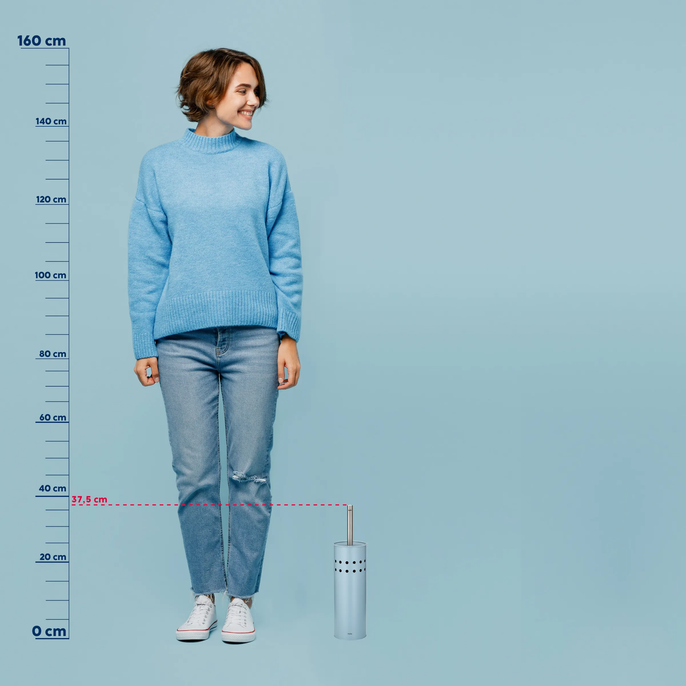 Junge Frau in hellblauem Strickpullover und zerrissenen Jeans steht neben einer weißen Bürste auf blauem Hintergrund.