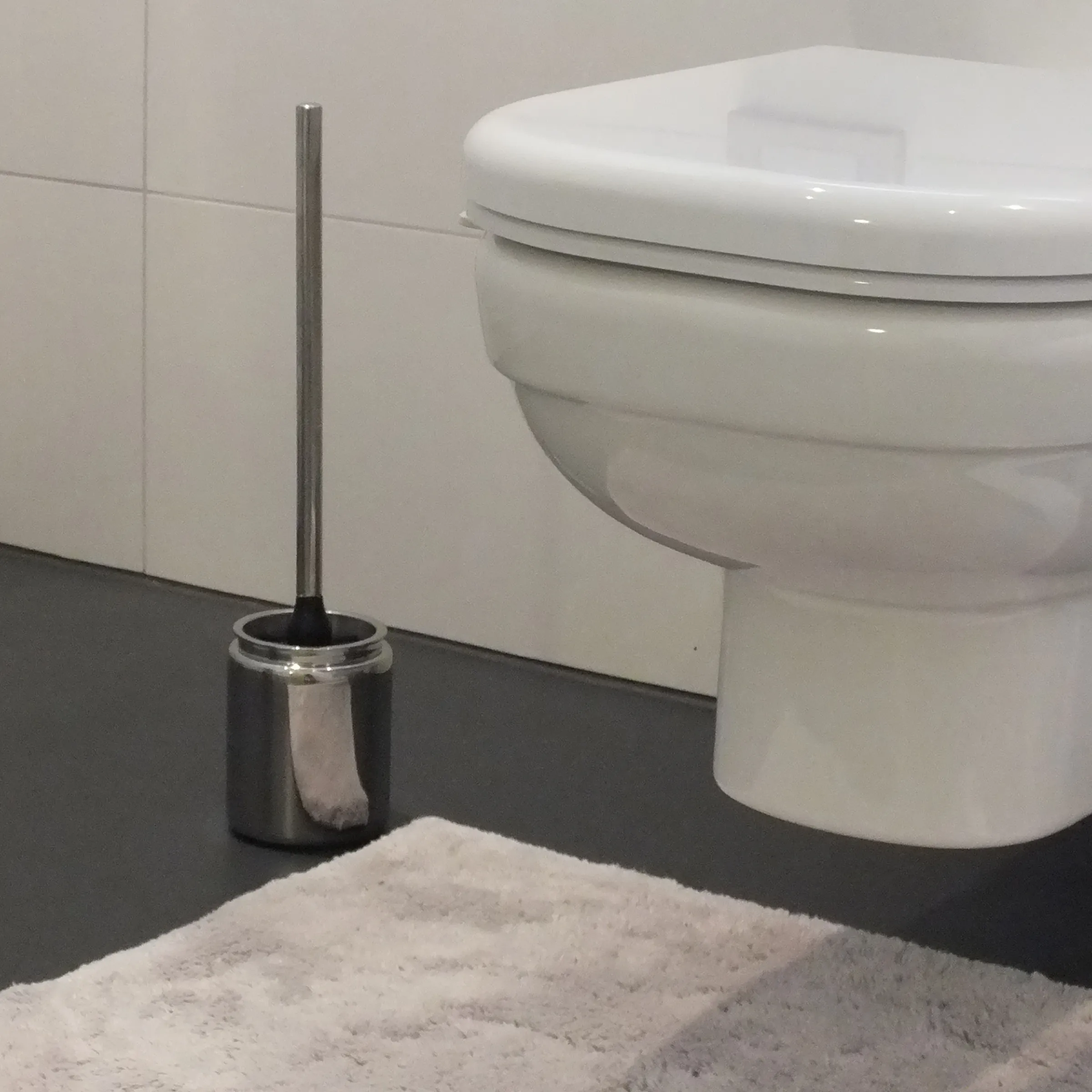 Toilettenbürste Edelstahl - Badezimmer Reinigung Toilettenbürste mit Edelstahlhalter neben weißem Klo und grauem Handtuch im modernen Badezimmer