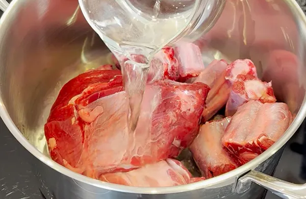 Fleisch auftauen in Schüssel mit Wasser - Küchenvorbereitung Rohes Fleisch in Edelstahlschüssel mit kaltem Wasser übergießen zum Auftauen oder Vorbereiten