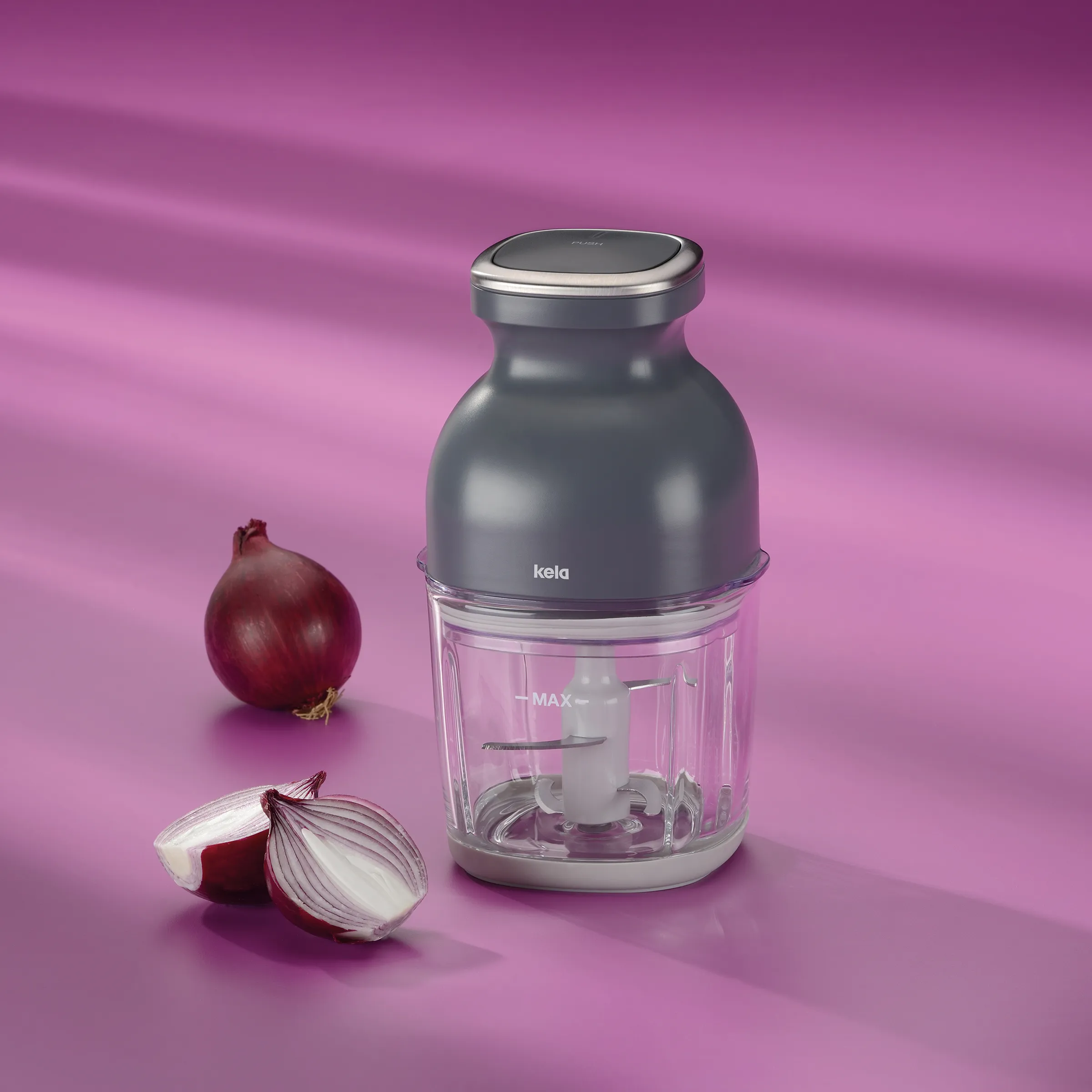 Kela Zerkleinerer mit transparentem Behälter und roten Zwiebeln auf violettem Hintergrund