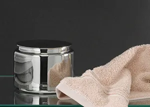 Transparenter Glasbehälter mit Metalldeckel neben beigefarbenem Handtuch auf grauem Hintergrund