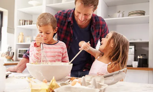 Vater und zwei Kinder backen zusammen in der Küche und rühren Teig in einer Schüssel um