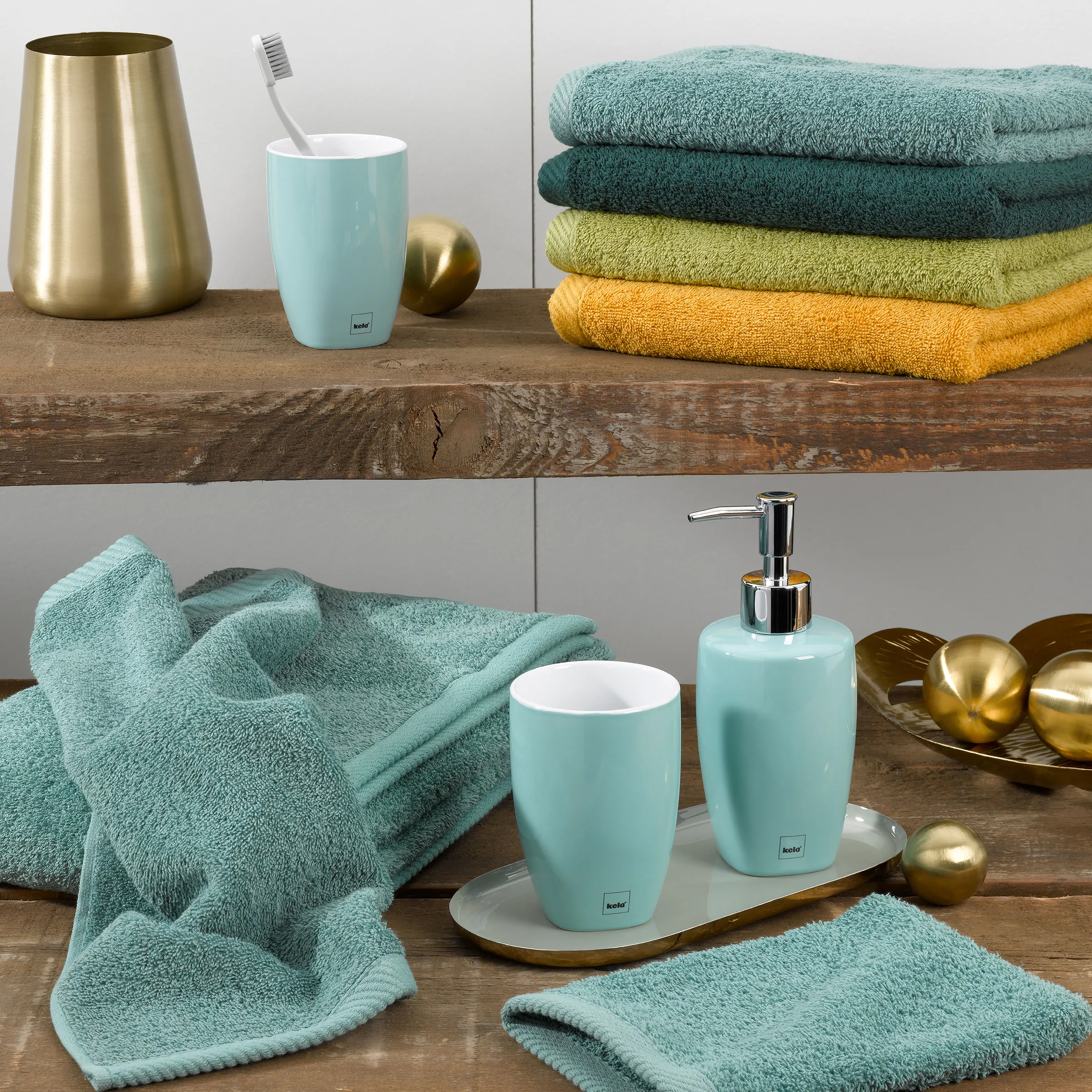 Badezimmer Accessoires Set türkis gold Badezimmer-Set mit türkisfarbenen Handtüchern, Zahnbürstenbecher, Seifenspender und goldfarbenen Accessoires auf Holzregal