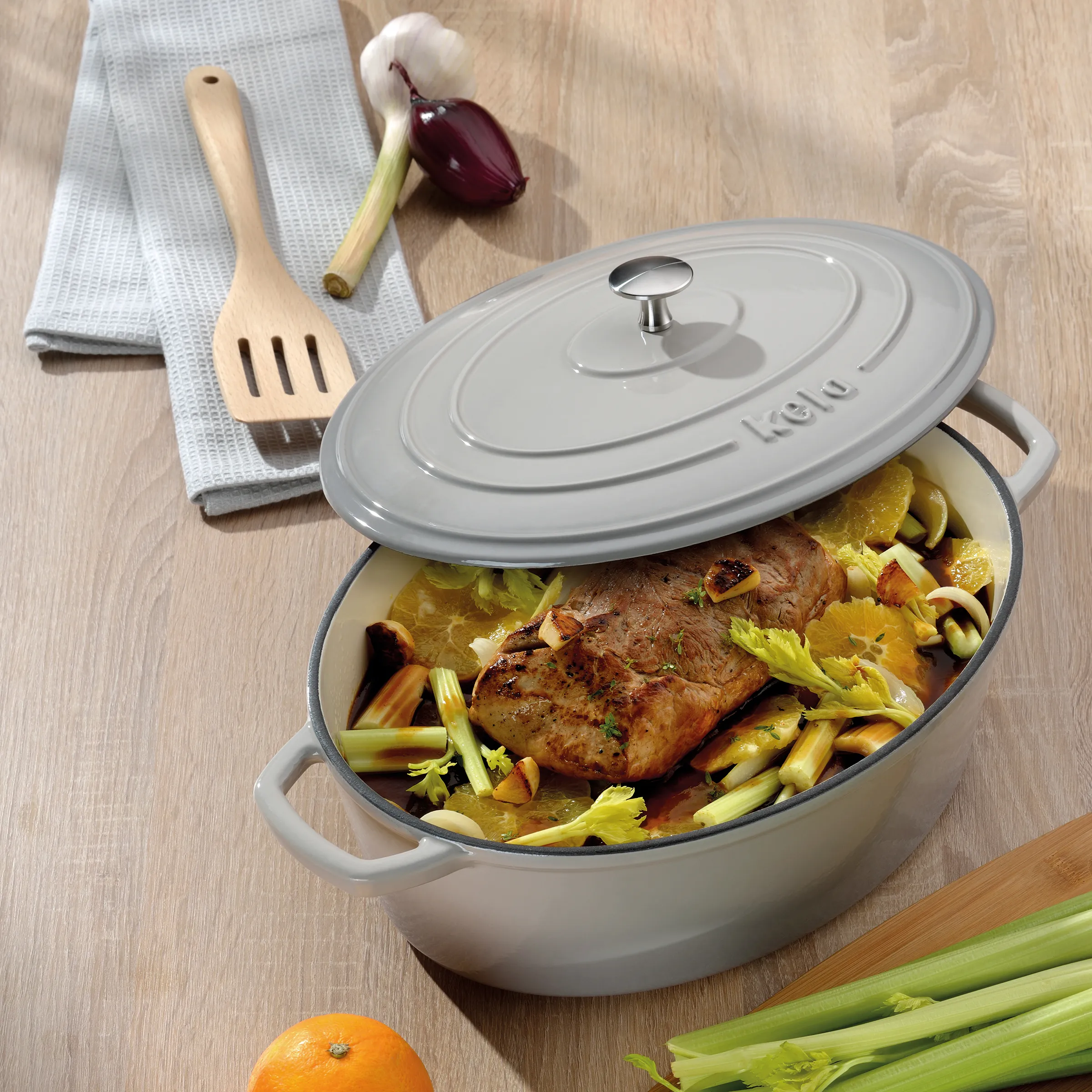 Staub Bräter oval mit Fleisch und Gemüse - Premium Gusseisen Schmortopf Staub Bräter mit Deckel enthält geschmortes Fleisch mit Gemüse auf Holztisch mit Kochutensilien