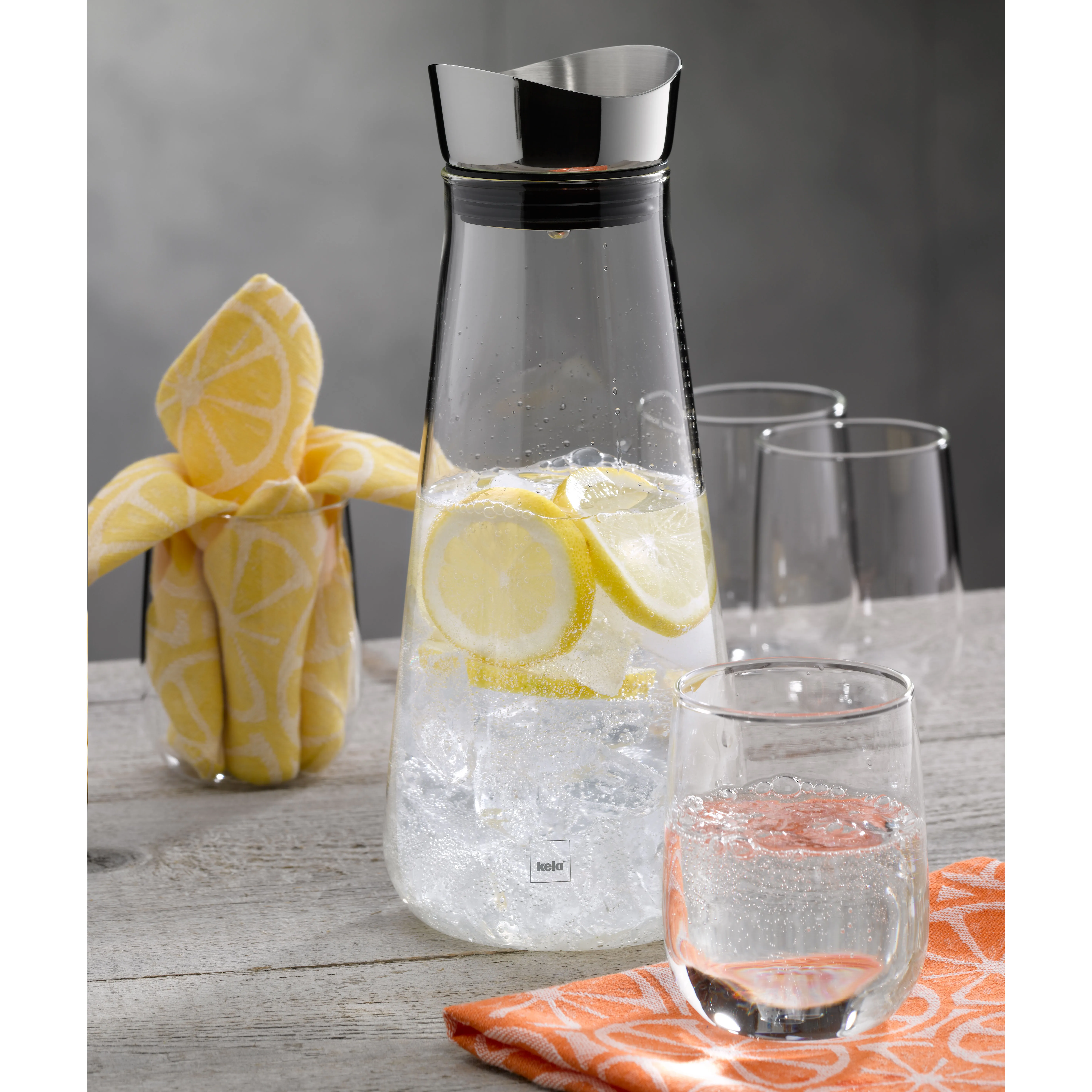 Glaskrug Wasserspender mit Zitrone und Eis Glaskrug mit Wasser, Zitronenscheiben und Eiswürfeln, daneben Gläser und frische Zitrone auf grauem Holztisch