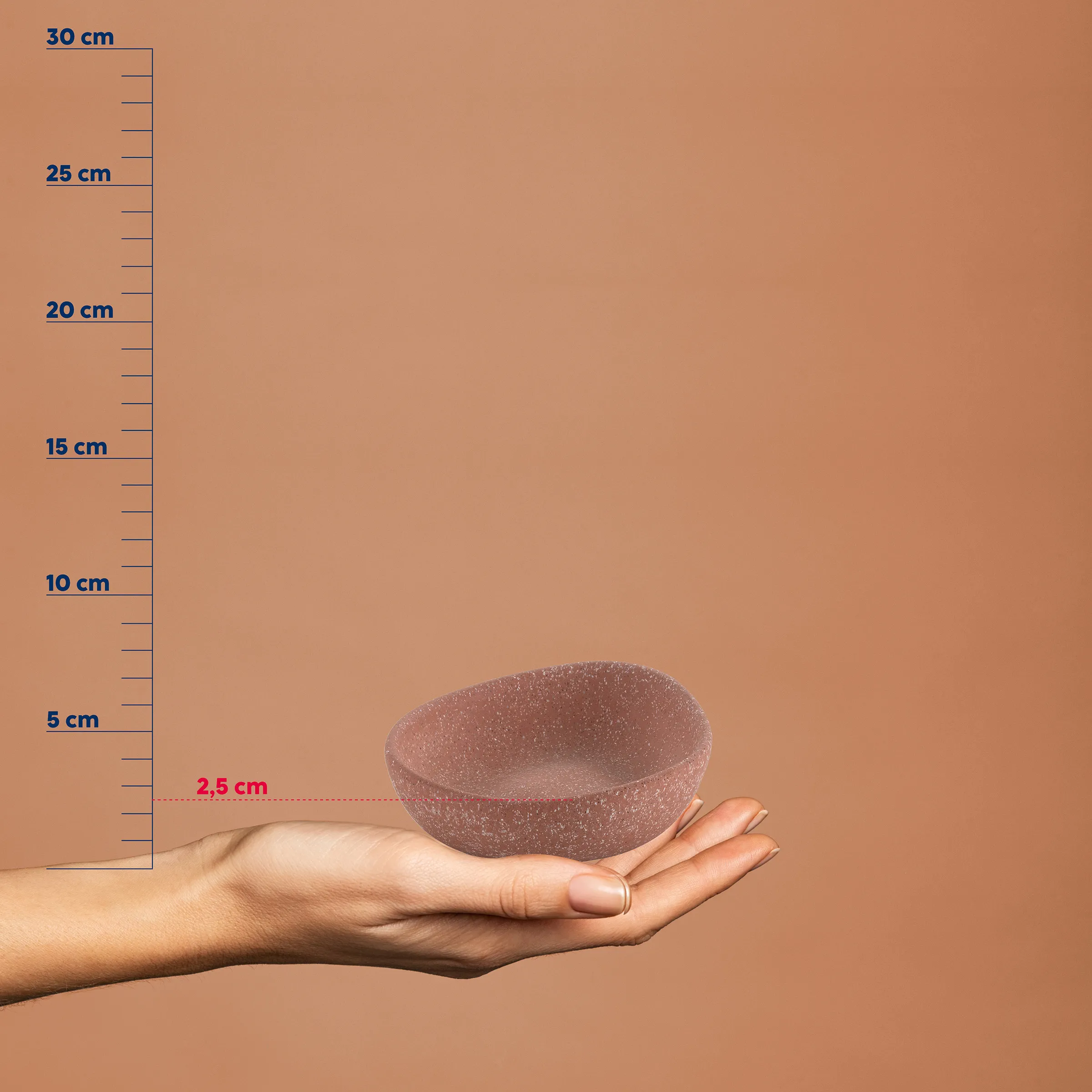 Kleine rosa körnige Schale in einer Hand, neben einer Messskala von 0 bis 30 cm, Größe etwa 2,5 cm