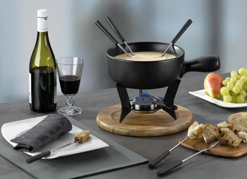 Käsefondue Set - Fondue Topf mit Zubehör Fondue-Set mit schwarzem Topf, Käsefondue, Weinflasche, Glas, Obst und Brot auf grauem Untergrund