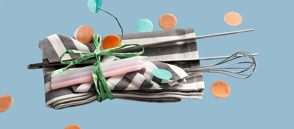 Küchenutensilien und Geschirrtücher - Dekoratives Küchenzubehör Set Küchenutensilien-Set mit gestreiften Geschirrtüchern, rosa Kerzen, Schneebesen und Holzlöffel auf hellblauem Hintergrund
