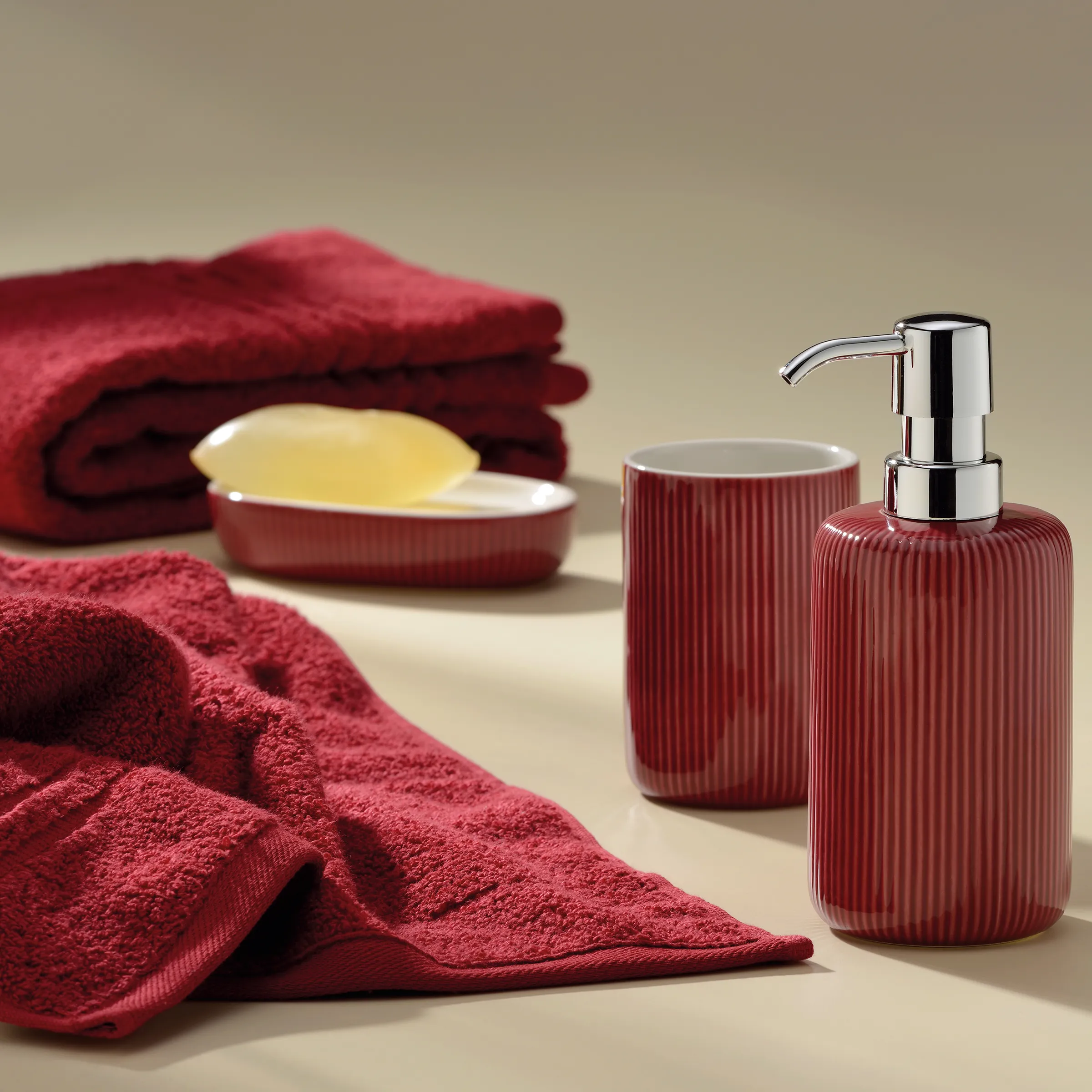 Badezimmer-Set Seifenspender Handtücher rot Badezimmer-Set mit roten Handtüchern, Seifenschale mit gelbem Stück, rotem Seifenspender und beigem Hintergrund