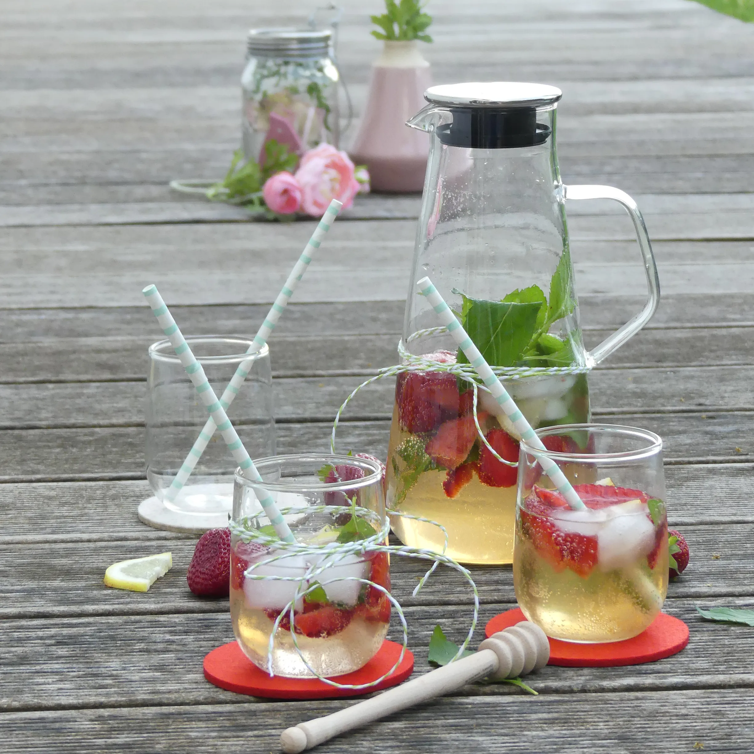 Erfrischende Erdbeer-Limonade mit Minze - Sommergetränk im Glas Erdbeer-Limonade mit Minze in Gläsern und Karaffe auf Holztisch, dekoriert mit Strohhalmen und roten Untersetzern