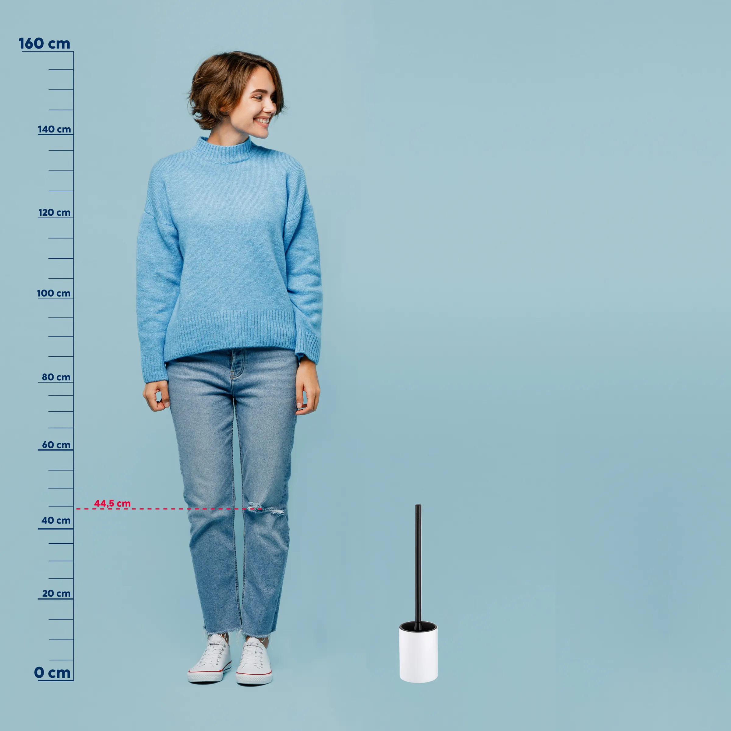 Toilettenbürste mit modernem Design - praktischer Badezimmer-Accessoire Frau in hellblauem Strickpullover und zerrissener Jeans steht neben einem weißen Toilettenbürsten-Behälter vor blauem Hintergrund.