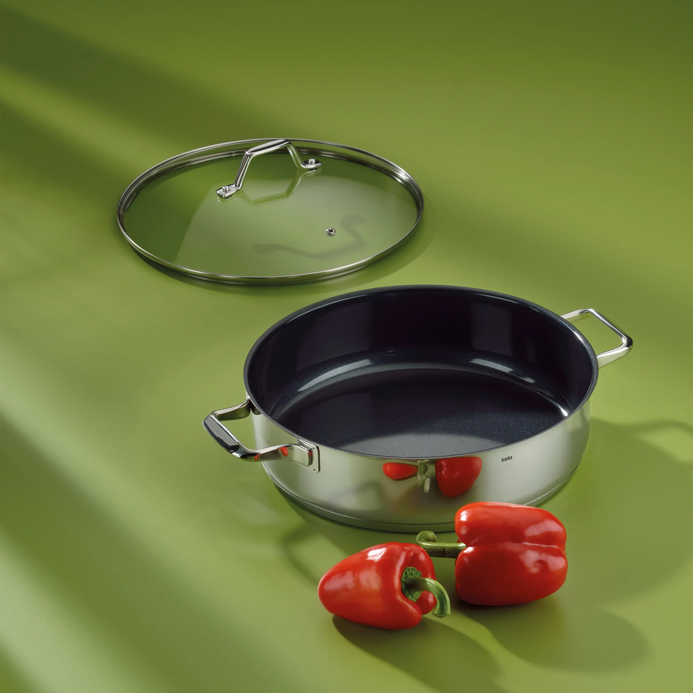 Bratpfanne Edelstahl mit Glasdeckel und Antihaftbeschichtung Große Edelstahl-Bratpfanne mit schwarzer Antihaftbeschichtung, Glasdeckel und roten Paprikaschoten auf grünem Untergrund