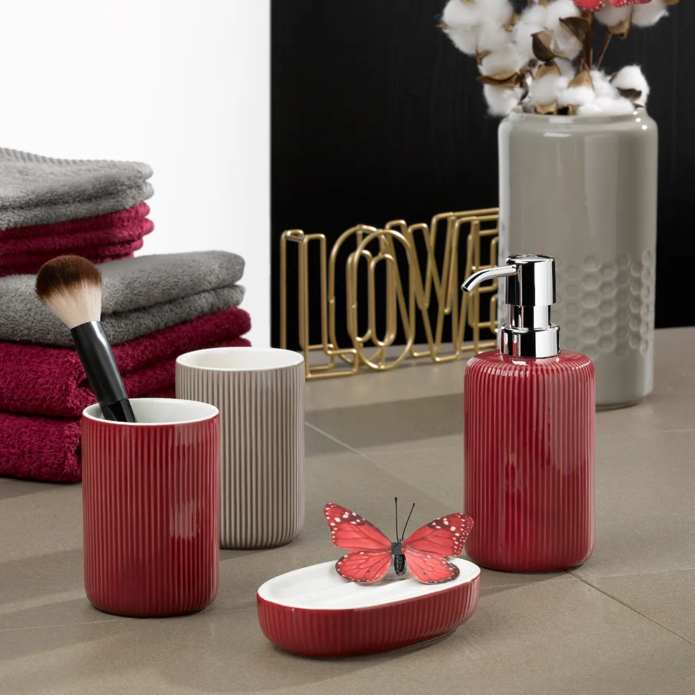 Ensemble d'accessoires de salle de bain moderne avec contenants en céramique côtelés rouges et gris, distributeur de savon, porte-savon papillon, serviettes et fleurs de coton en vase.
