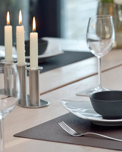 Tischgedeck elegant - Tischdekoration mit Kerzen Elegant gedeckter Tisch mit brennenden Kerzen in silbernen Kerzenständern, Weingläsern, schwarzen Schüsseln und Besteck auf grauem Platzset.