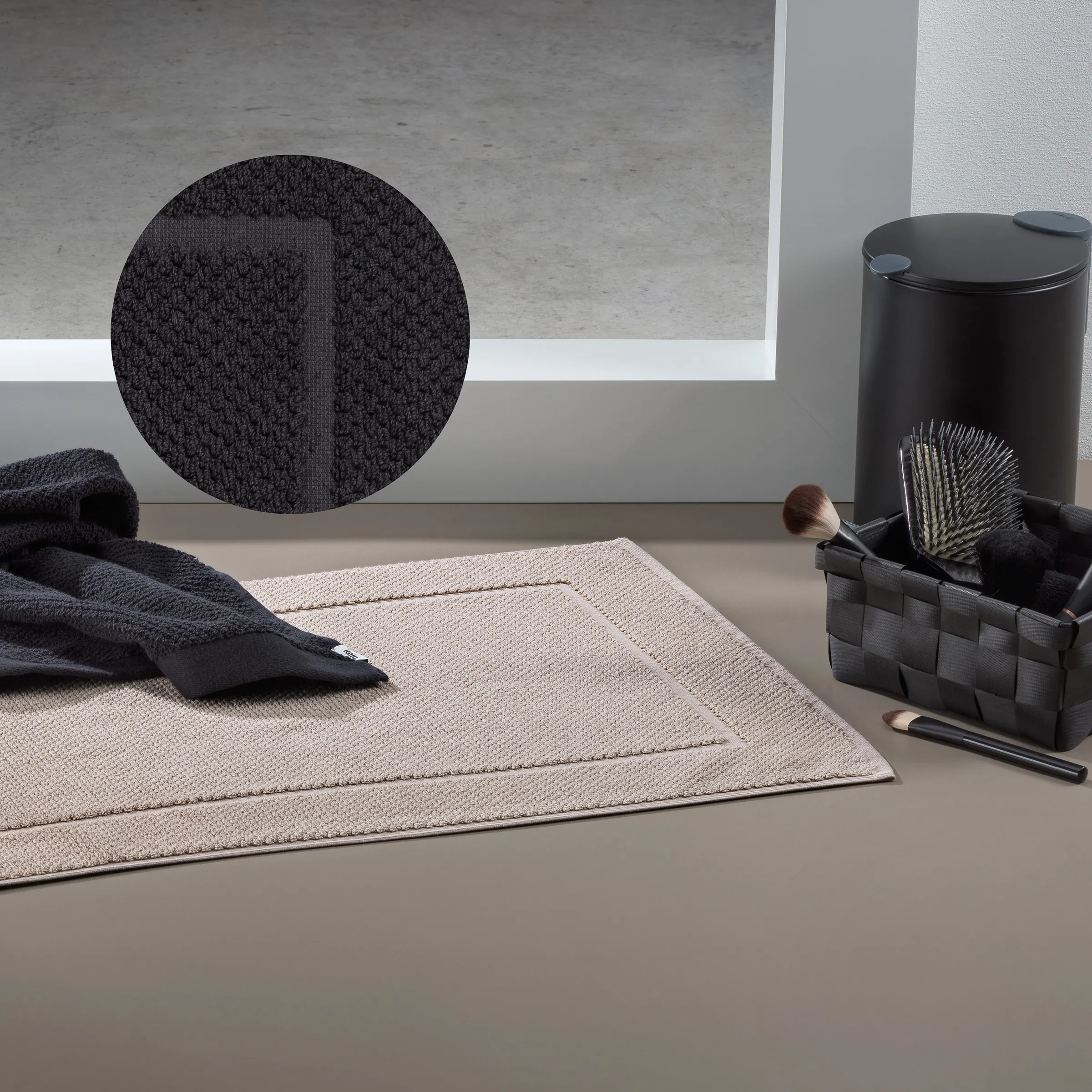 Beauty- und Badezimmer-Accessoires Set mit Handtuch und Haarbürsten Flache Produktansicht mit beigefarbenem Handtuch, schwarzem Haarbürsten-Set in Korb und schwarzem Texturedetail-Kreis auf grauem Hintergrund