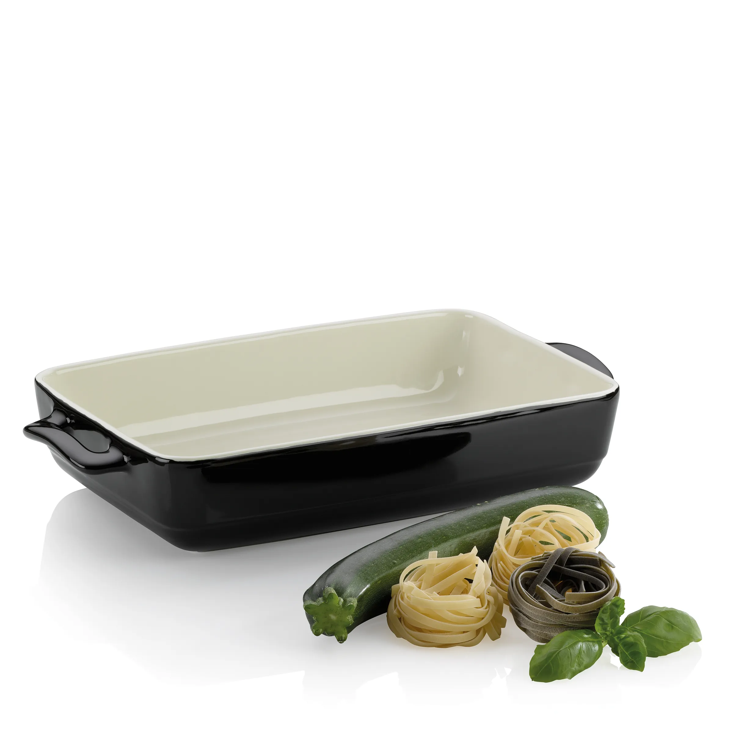 Auflaufform schwarz – Backform für Gemüse und Pasta Schwarze Auflaufform mit cremefarbenem Innenbereich neben Zucchini, Pasta und frischem Basilikum